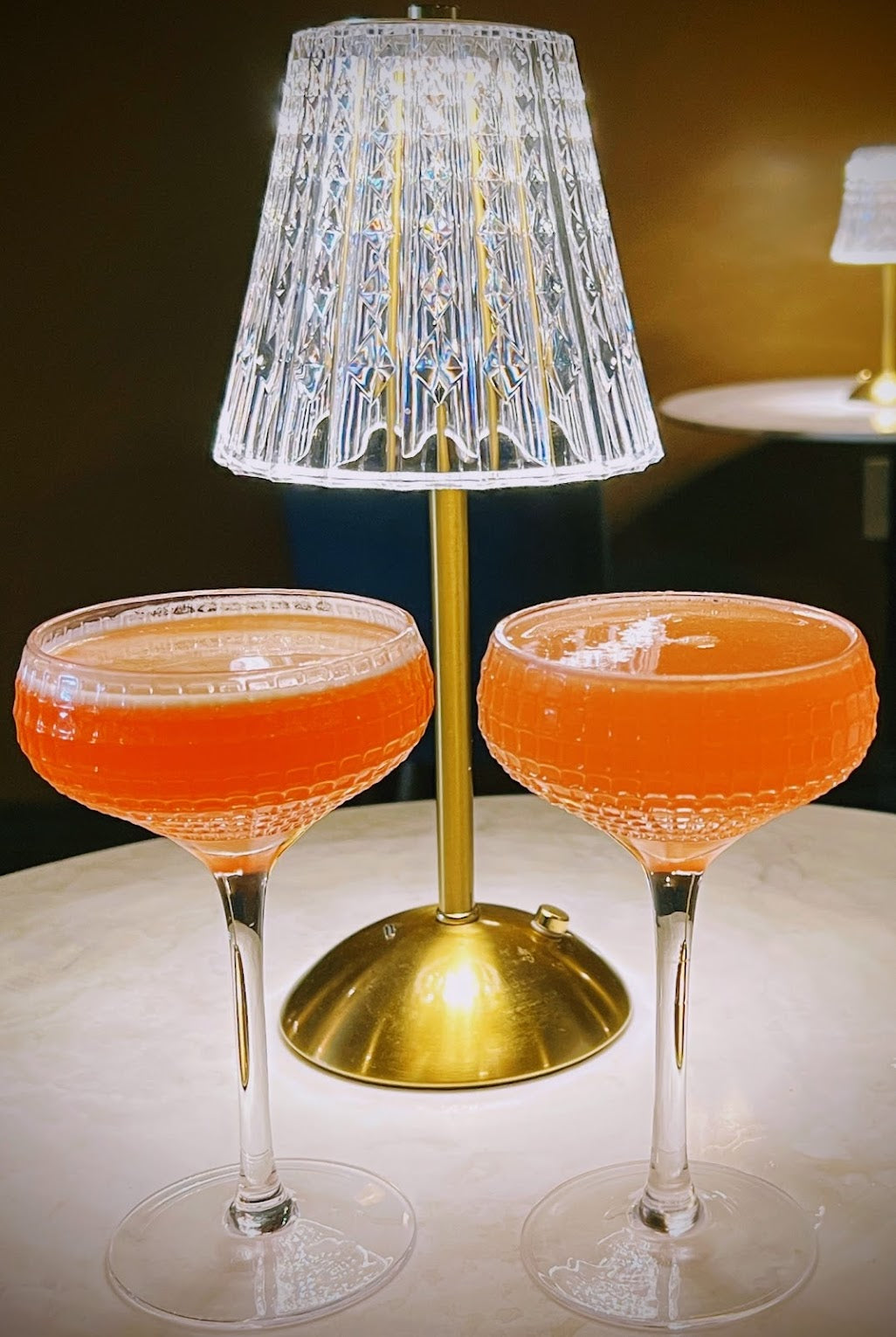 Two Olivino craft cocktails beside a glowing table lamp